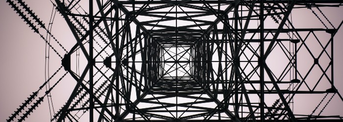 Looking up the intricate geometric structure of a tall powerline tower, framed against a soft pink sky.